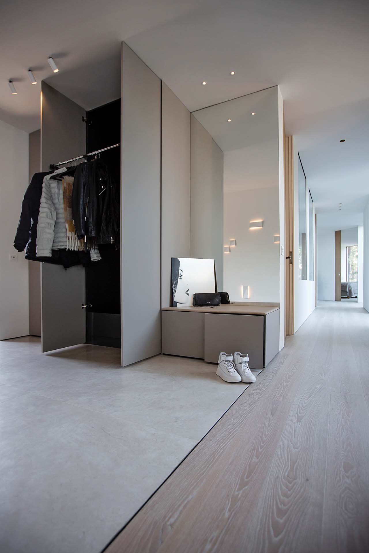 Stiligt - Modern hall med en öppen garderob med jackor, en bänk med spegel och väska och vita sneakers placerade på golvet bredvid.