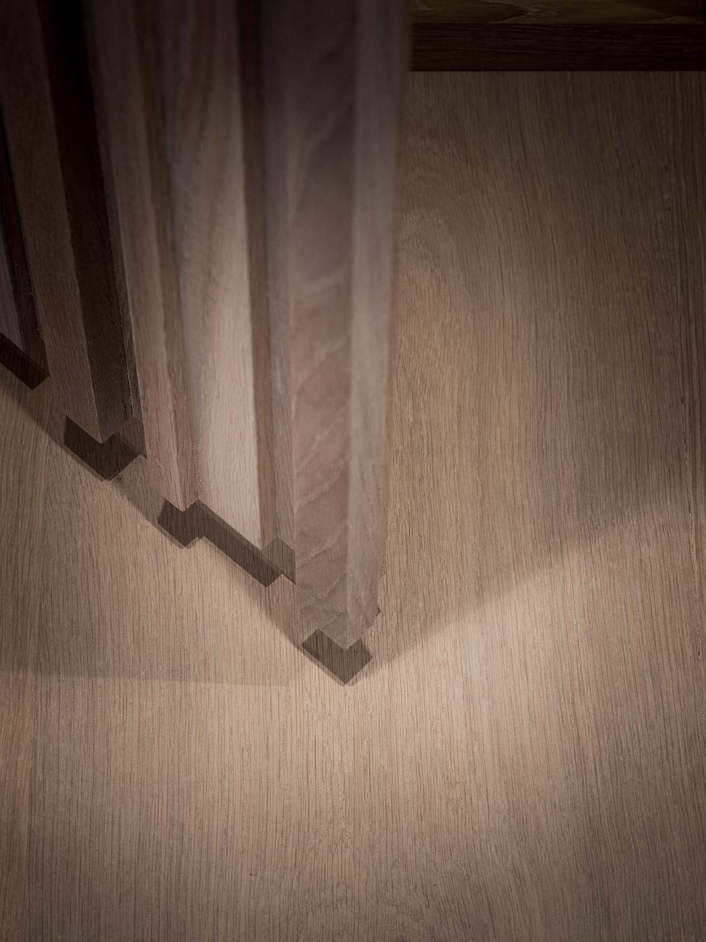 Stiligt - Vertikala träribbor som kastar geometriska skuggor på ett ljust trägolv, sett från ovan.