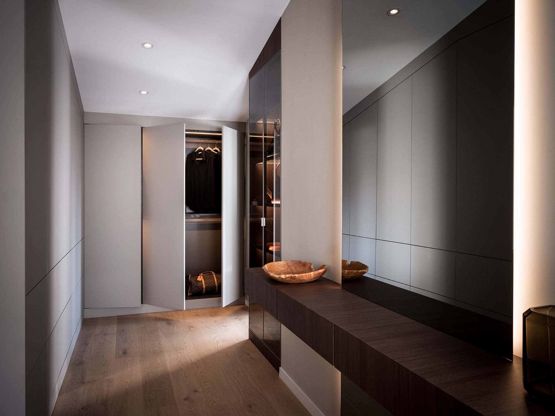 Stiligt - En modern, minimalistisk klädkammare med inbyggda garderober, trägolv, en lång bänk i mörkt trä och infälld belysning.