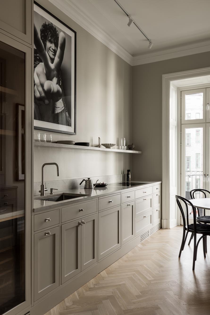 Stiligt - Minimalistisk kök i shakerstil med ljusgrå skåp, vägghängd hylla och ett stort svartvitt foto ovanför diskbänken; ett runt bord och stolar sitter nära ett högt fönster.