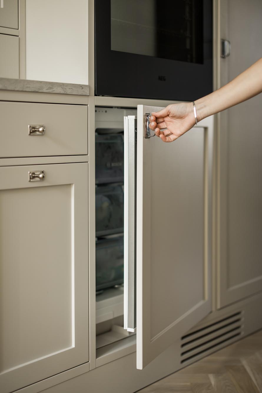 Stiligt - En persons hand som öppnar en beige inbyggd fryslåda i en modern kök i shakerstil.