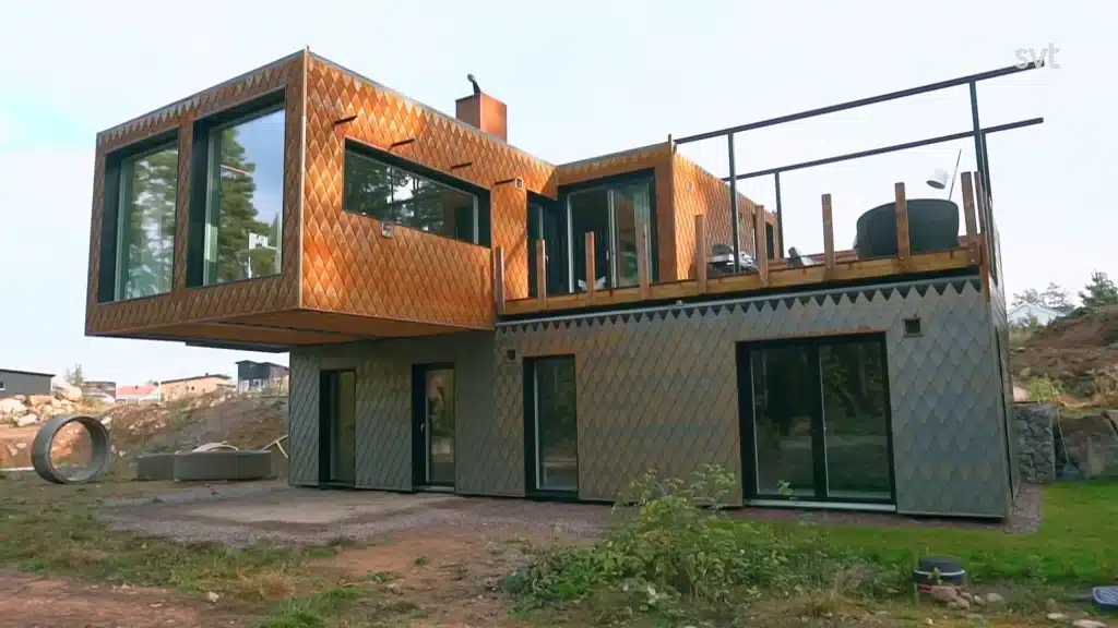 Stiligt - Ett modernt tvåvåningshus med stora glasfönster och geometriskt mönstrade exteriörpaneler, med en övre våning med en fribärande sektion och en balkong.