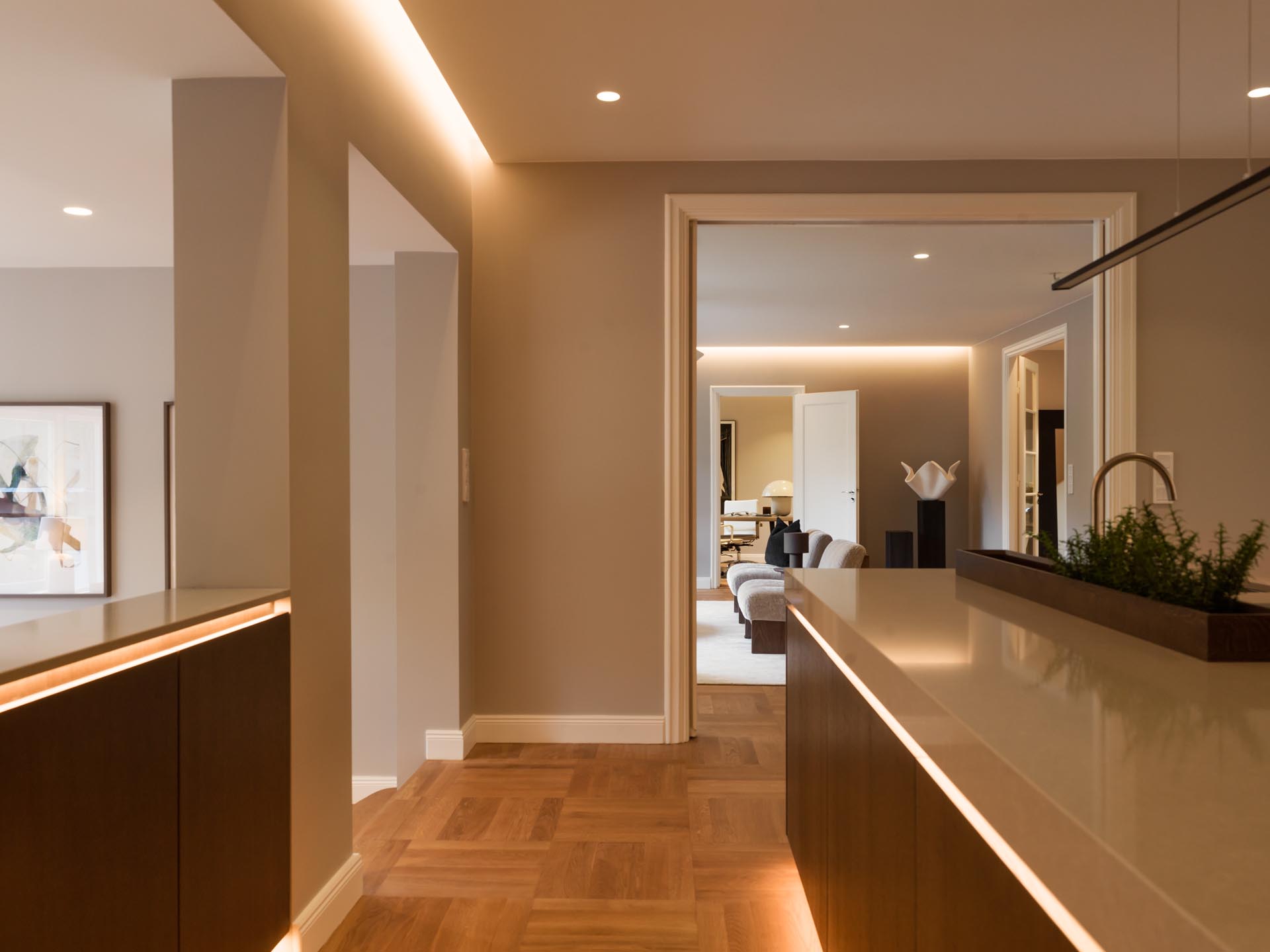 Stiligt - Modern inre hall med trägolv, beiga väggar, infälld belysning och utsikt mot ett vardagsrum med soffa och prydnadsföremål, sömlöst ansluten till en träkök med pocketdörrar för extra elegans.