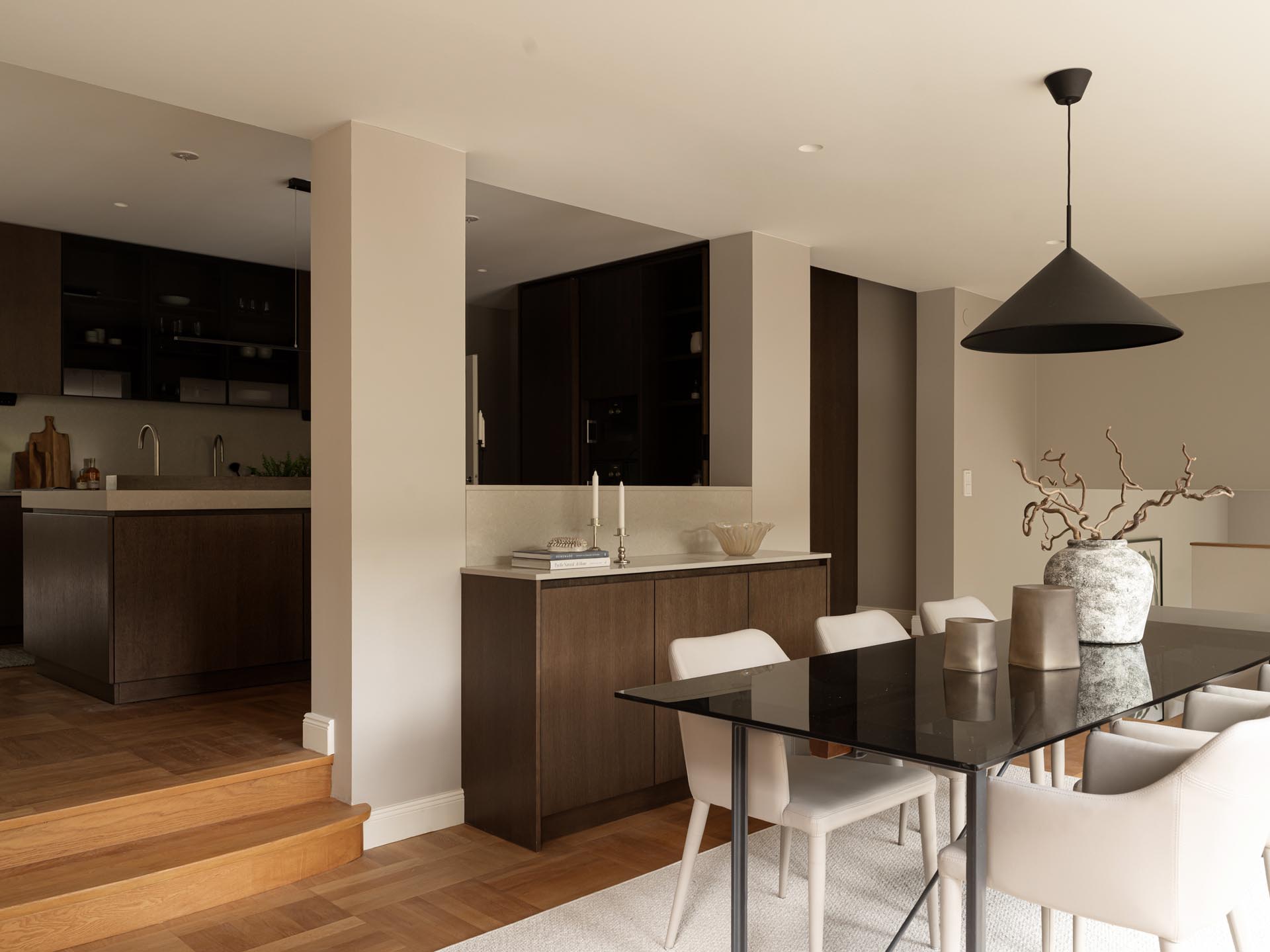 Stiligt - Modern öppen planlösning träkök med pocketdörrar och matplats med mörkt träskåp, svart matbord, vita stolar och minimalistisk inredning. En stor taklampa hänger ovanför bordet.