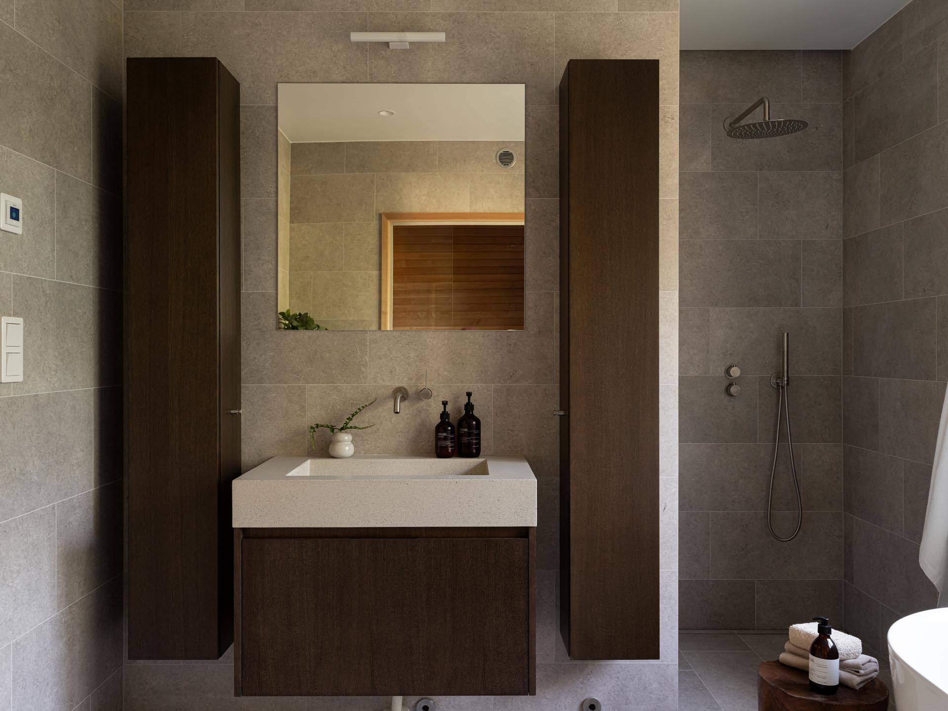 Stiligt - Modernt badrum med svävande handfat, rektangulär spegel, två höga skåp och en duschkabin med regndusch – perfekt komplement till en träkök med pocketdörrar för en sömlös modern hemdesign.