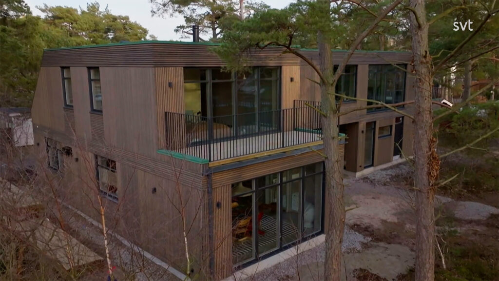 Stiligt - Ett modernt tvåvåningshus med stora glasfönster och träexteriör, omgivet av träd i en naturlig miljö.