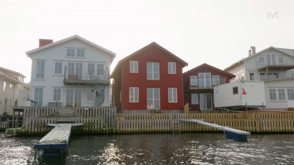 Stiligt - Tre hus vid vattnet, inklusive ett rött i mitten, står sida vid sida med träbryggor som sträcker sig över vattnet.