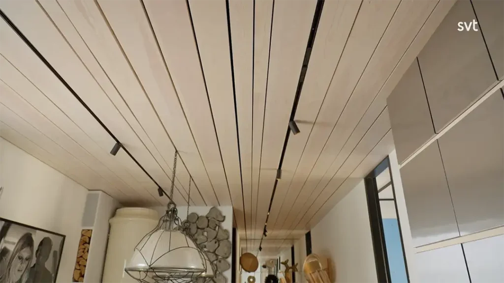 Stiligt - Modern interiör med ett ljust träpanel i taket, spårbelysning, hängande taklampa, väggkonst, staplad ved och synliga köksredskap.