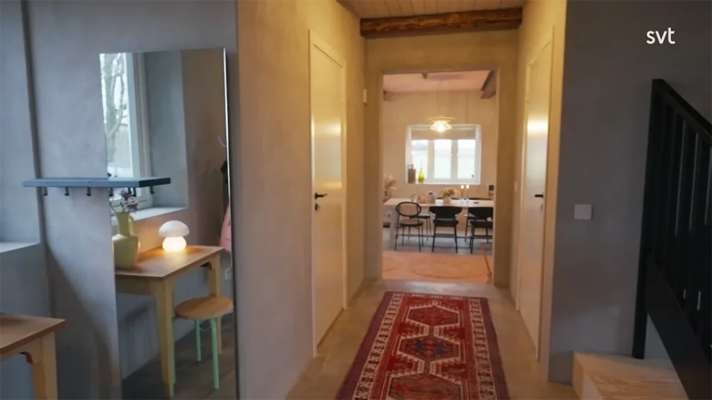 Stiligt - En hall med en rödmönstrad Kverrestad löparmatta leder till en matplats. Ett litet bord med lampa och spegel är till vänster, medan trappor är till höger.