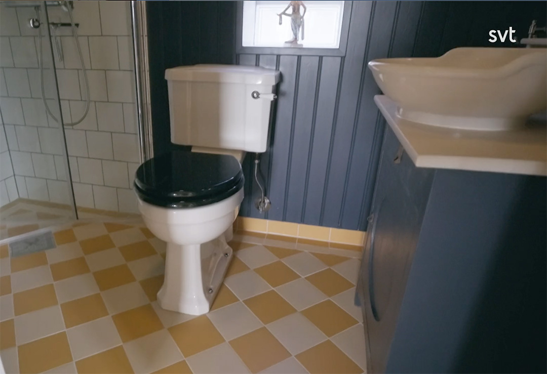 Stiligt - Ett badrum med toalett, vitt handfat på mörkt handfat och gul-vitrutigt klinkergolv som sätter en lekfull Grönalund-inspirerad touch.